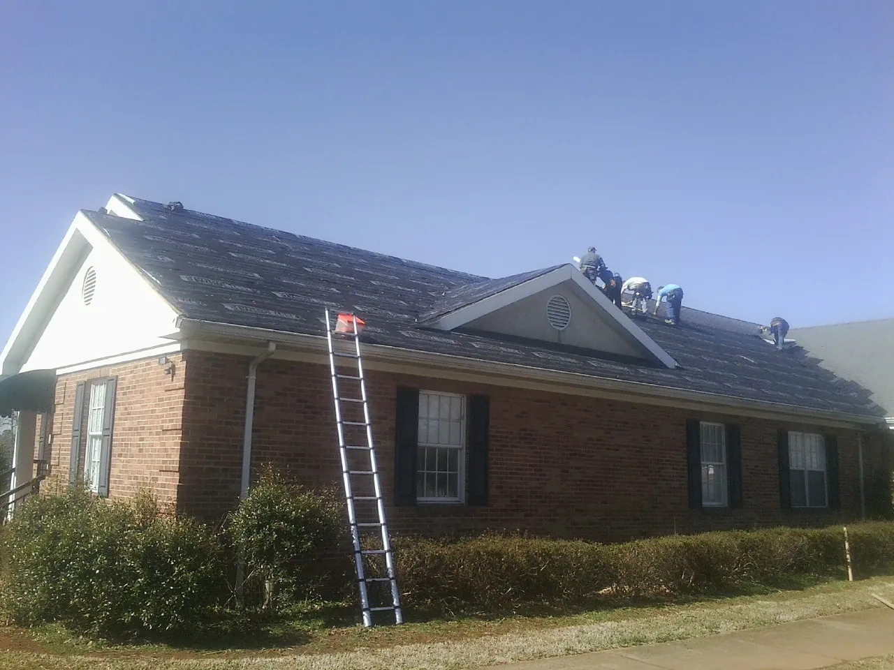 Crew tearing shingles off a brick ranch roof with a ladder set — Emergency Roof Repair work by our crew in Annawan