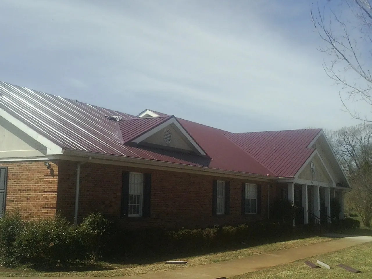 Red metal roof with gabled entries on a long brick building, from a Hail Damage Roof Repair job in Annawan
