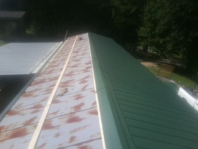 Old rusted panels beside newly installed green metal roofing — Wind Damage Roof Repair by Roofing Brothers in Annawan