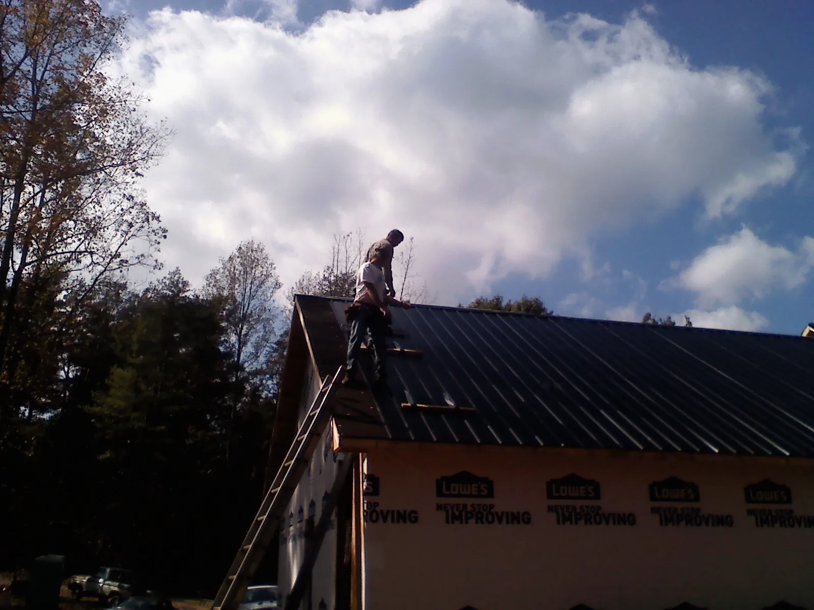 Roofer fastening dark metal panels high against a cloudy sky, from a Roof Inspection job in Annawan